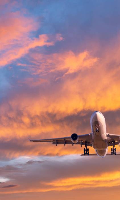 Airplane is flying in colorful sky at sunset. Landscape with passenger airplane, blue sky with orange and pink clouds. Aircraft is landing. Business and commercial. Travel. Aerial view. Transport